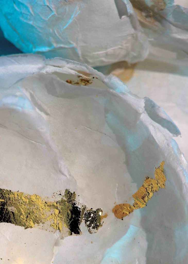 Close up of bowls made of rice paper mâché and 23 Carat gold leaf reflected on a bright blue surface. Part of the Homage process, a self-care practice created by Marie Barincou for nurses and oncology staff to address the loss of their patients.