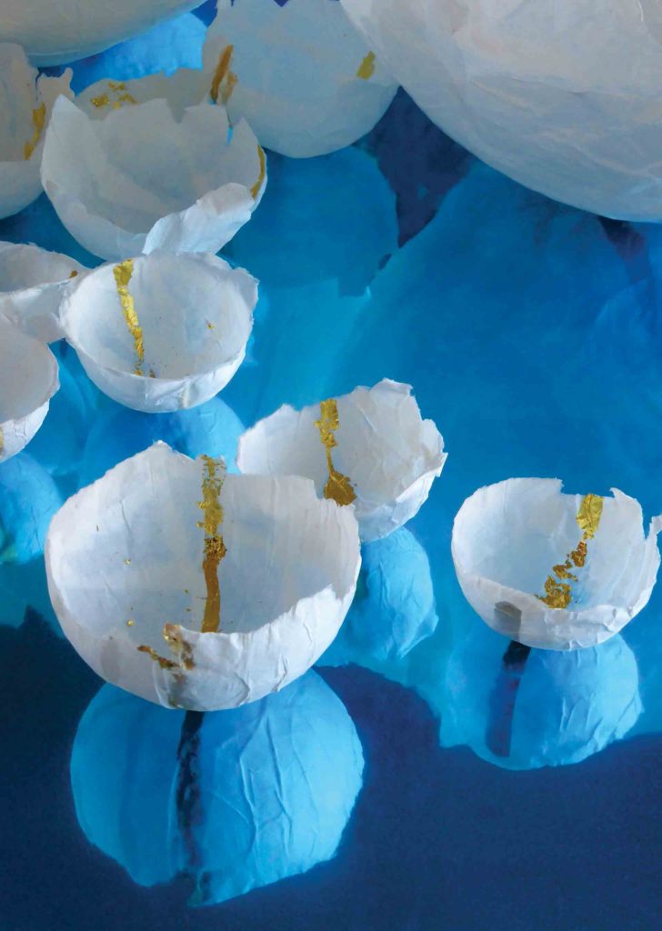 White bowls made of rice paper mâché and 23 Carat gold leaf reflected on a bright blue surface. This is part of the Homage process, a self-care practice created by Marie Barincou for nurses and oncology staff to address the loss of their patients.