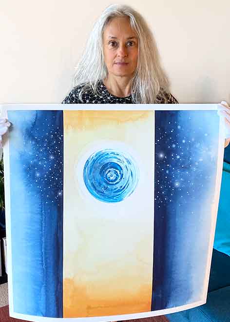 Marie Barincou, Artist and Creative Arts Therapist is holding her 76 cm square painting "Behind" from the series JOURNEYS displayed at Canberra Public Hospital Oncology Ward. There are 3 vertical strips in the painting, 2 are night blue with stars while the middle one is yellow with a blue planet in its upper part.